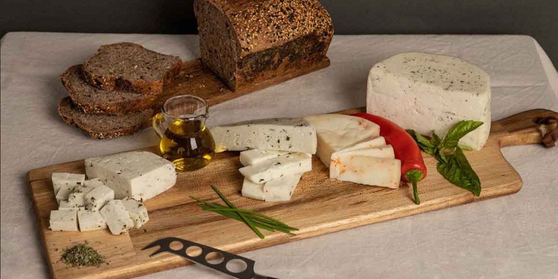 Variedad de quesos artesanos chilenos con hierbas y ají, acompañados de pan integral y aceite de oliva sobre tabla