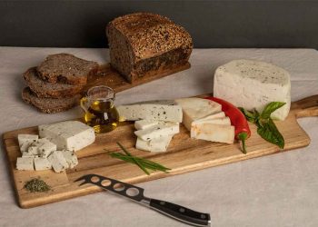 Variedad de quesos artesanos chilenos con hierbas y ají, acompañados de pan integral y aceite de oliva sobre tabla