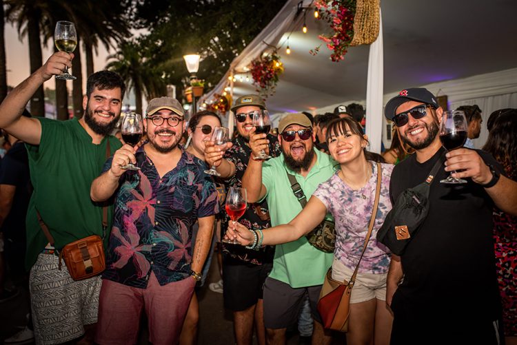 Grupo de jóvenes brindando con vino tinto y blanco en una animada fiesta de la vendimia en Chile, celebrando la cosecha 2026 al aire libre al atardecer.